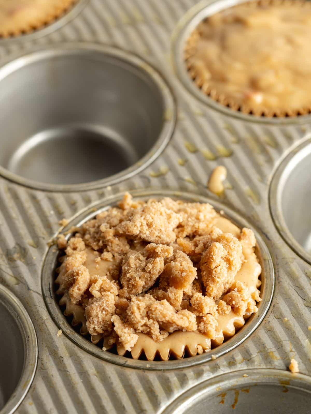 apple muffins with crumble topping in a muffin pan before baking.