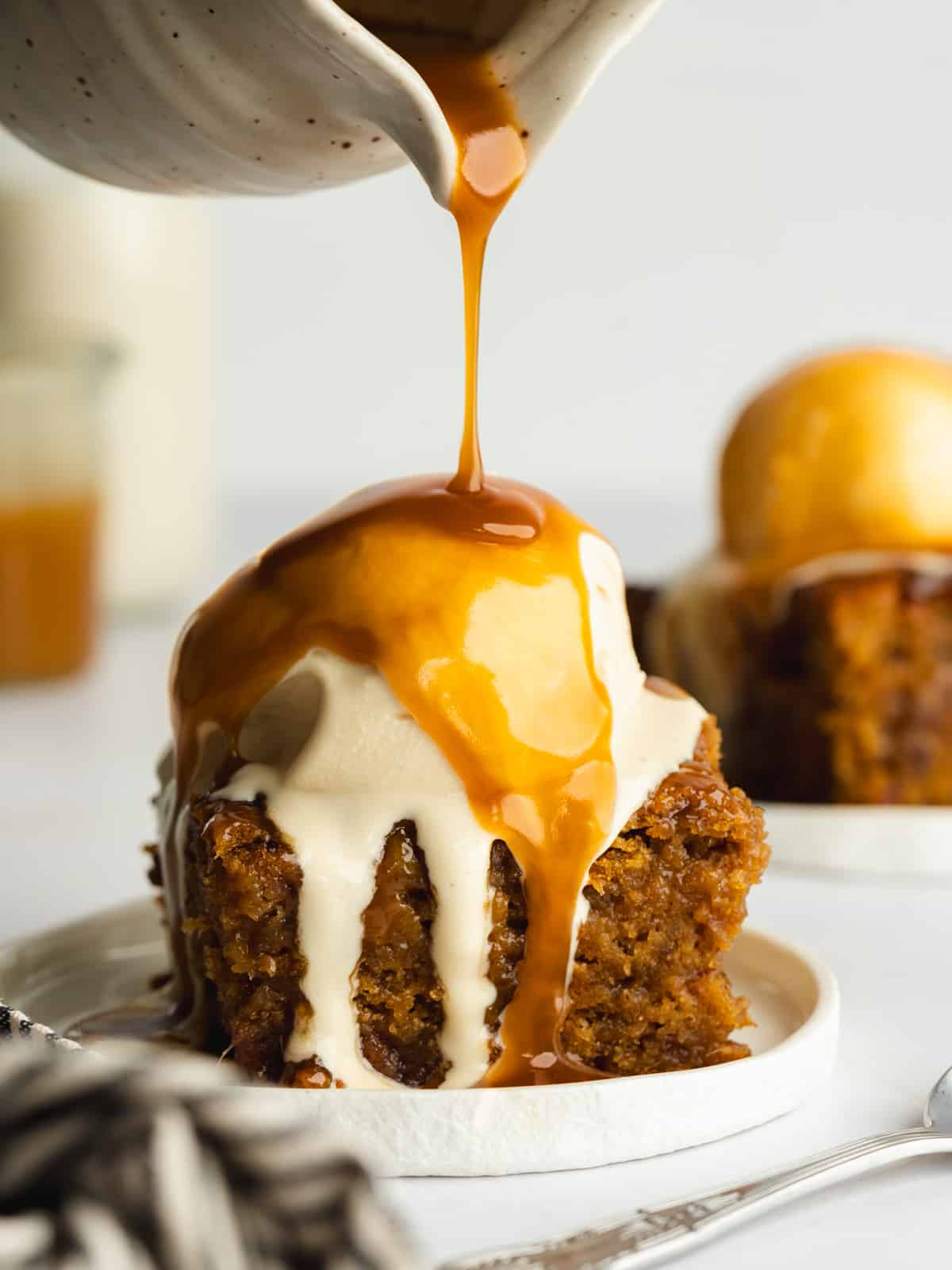 pouring warm toffee sauce over date pudding with a scoop of ice cream on top.