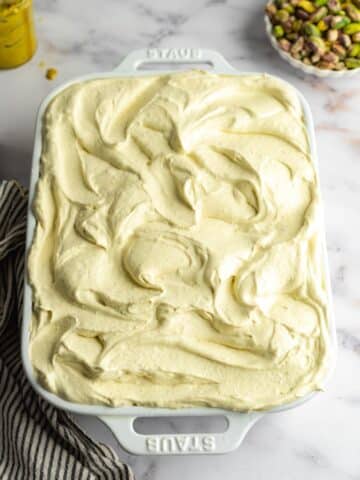 pistachio three milk cake in a staub pan with pistachio whipped cream.