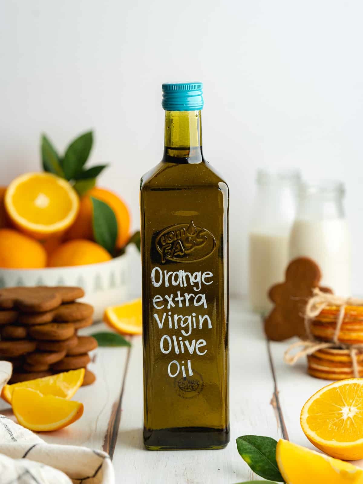 a bottle of labeled orange extra virgin olive oil with gingerbread cookies and fresh oranges scattered around.