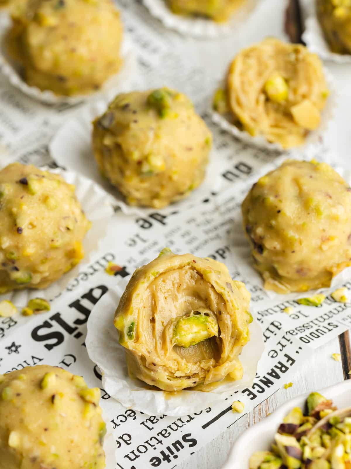 homemade pistachio chocolate truffles on newspaper with a bite taken from one of them.