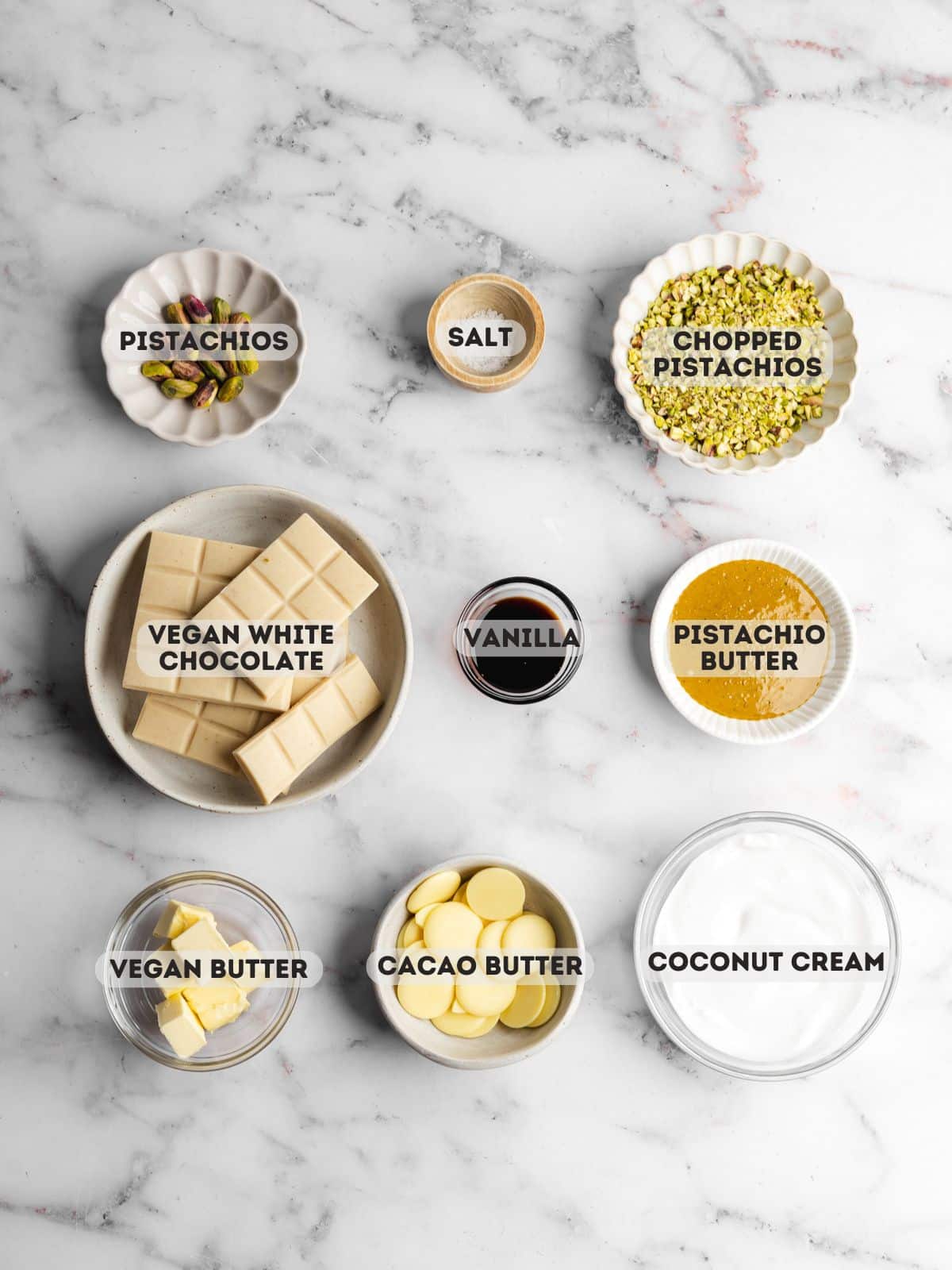 ingredients for pistachio chocolate truffles measured out in bowls on a marble surface.