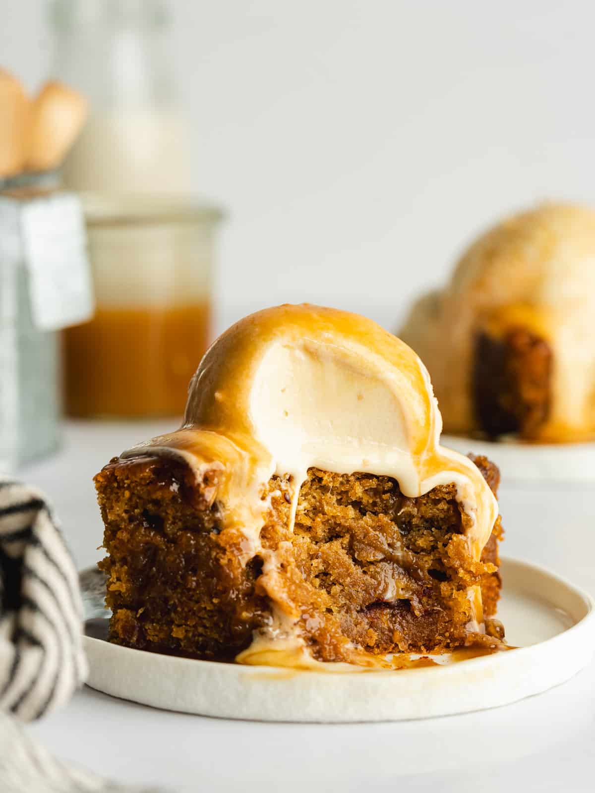 a portion of date pudding on a plate with a scoop of ice cream and toffee sauce and a spoonful taken from it.