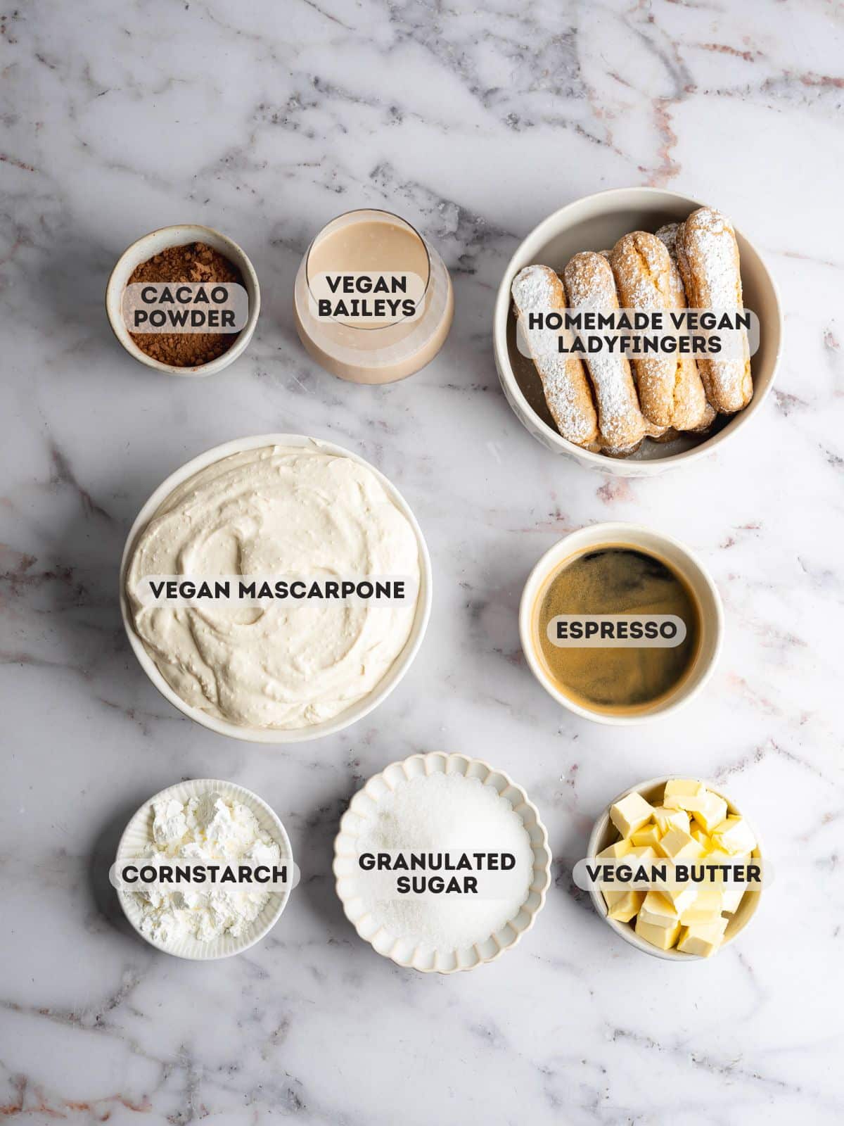 ingredients for vegan baileys tiramisu measured out in bowls on a marble gray surface.