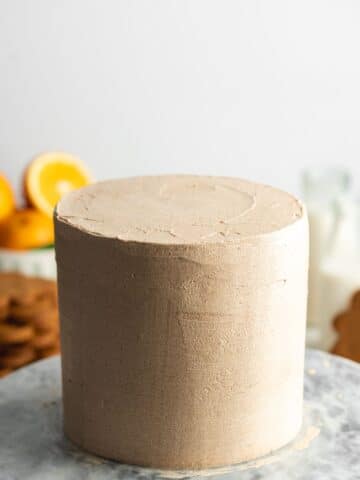 a gingerbread layer cake frosted with brown sugar buttercream on a marble cakestand.