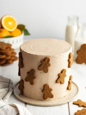 a lightly frosted gingerbread cake on a ceramic plate with plain gingerbread men stuck around the sides of the cake.