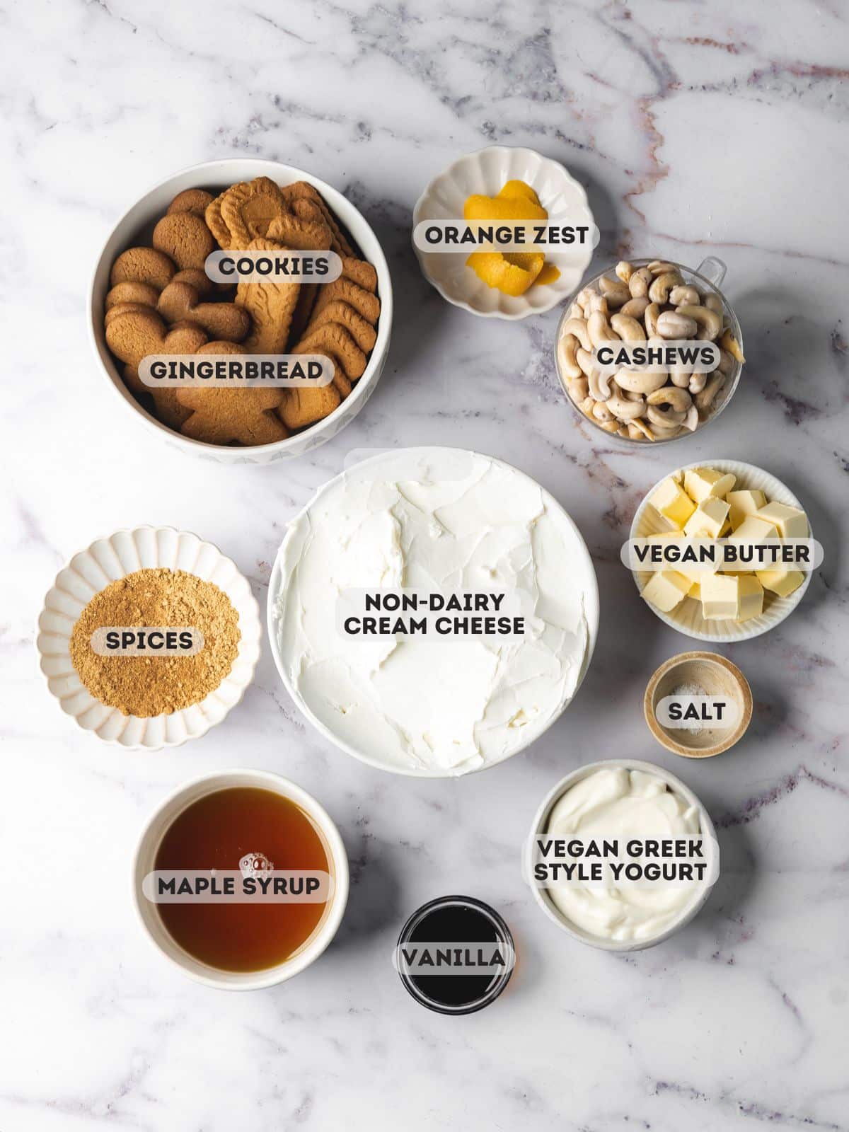 ingredients for vegan gingerbread cheesecake measured out in bowls on a marble surface.