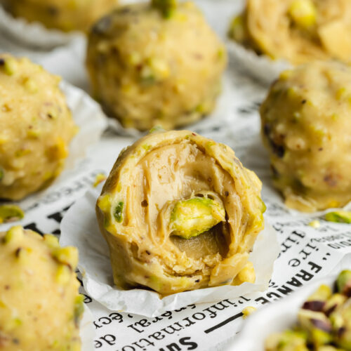 pistachio ferrero rocher-style truffles on newspaper with a bite taken from one showing the creamy ganache filling.