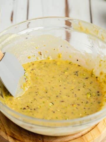 melted white chocolate, pistachio butter and chopped pistachios in a glass bowl.