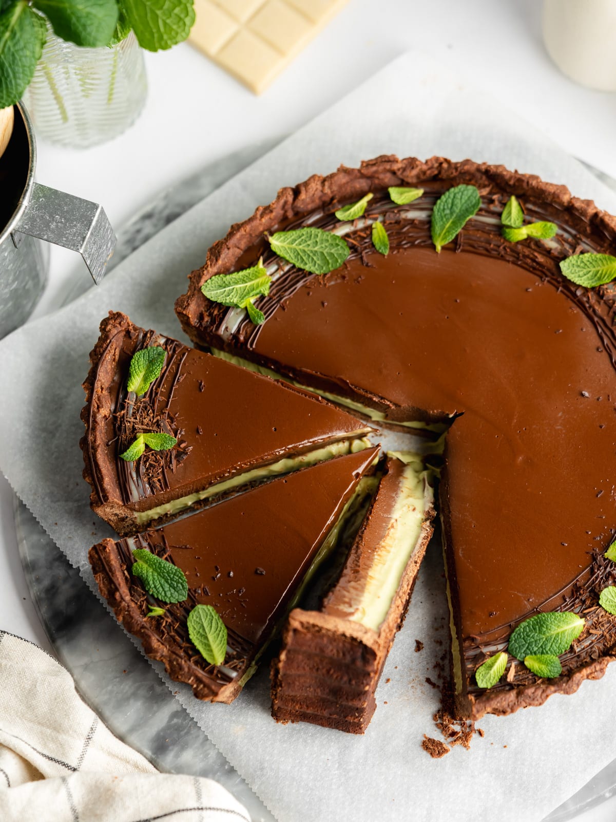 a layered dark chocolate and mint ganache tart with a few slices cut and fresh mint leaves on top.