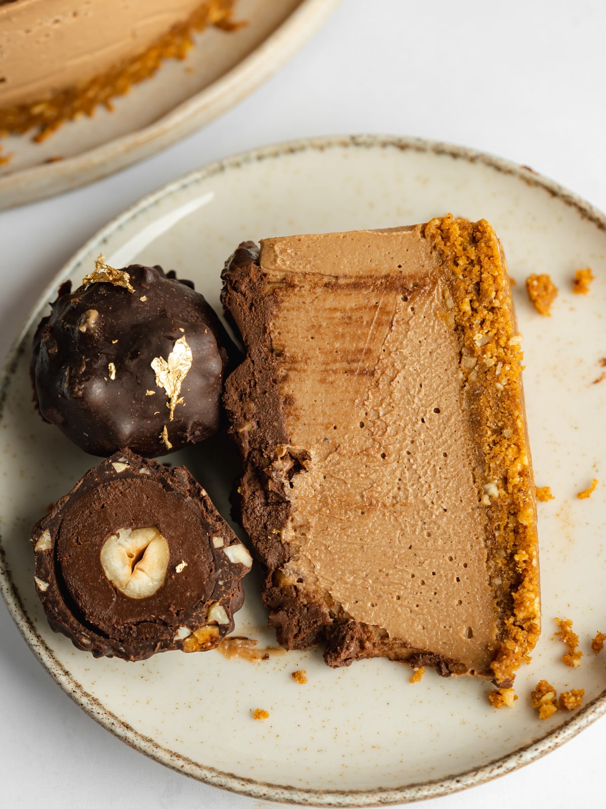 a slice of ferrero rocher cheesecake on a small plate with 2 homemade truffles on top.