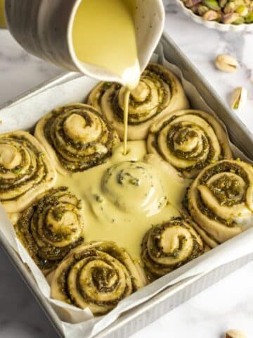 pouring pistachio cream over pistachio rolls before baking.
