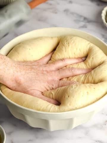 a hand punching the air out of a bowl of bread dough.