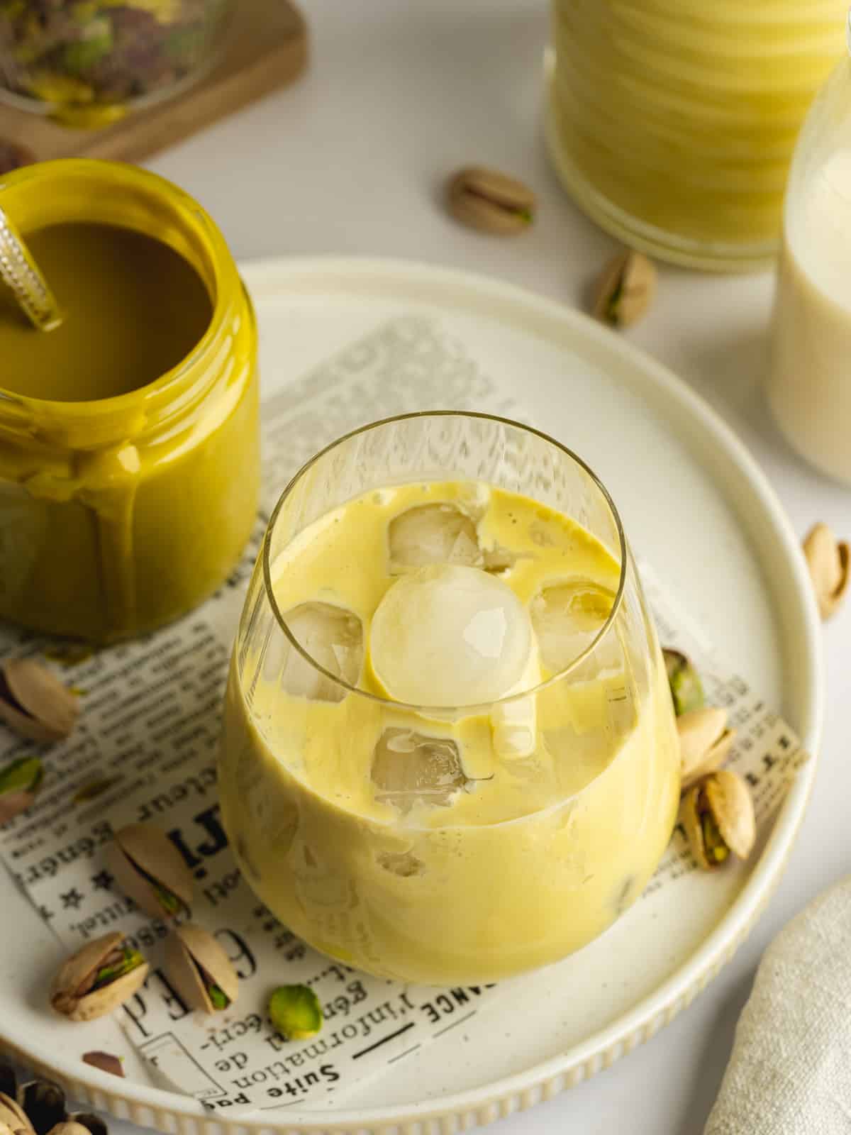 a glass of pistachio cream liqueur with ice and pistachio nuts scattered around it.