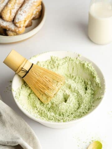 matcha powder and powdered sugar mixed with a matcha whisk in a small bowl.