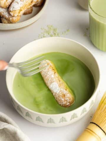 ladyfinger cookie being dipped into a bowl with matcha latte.