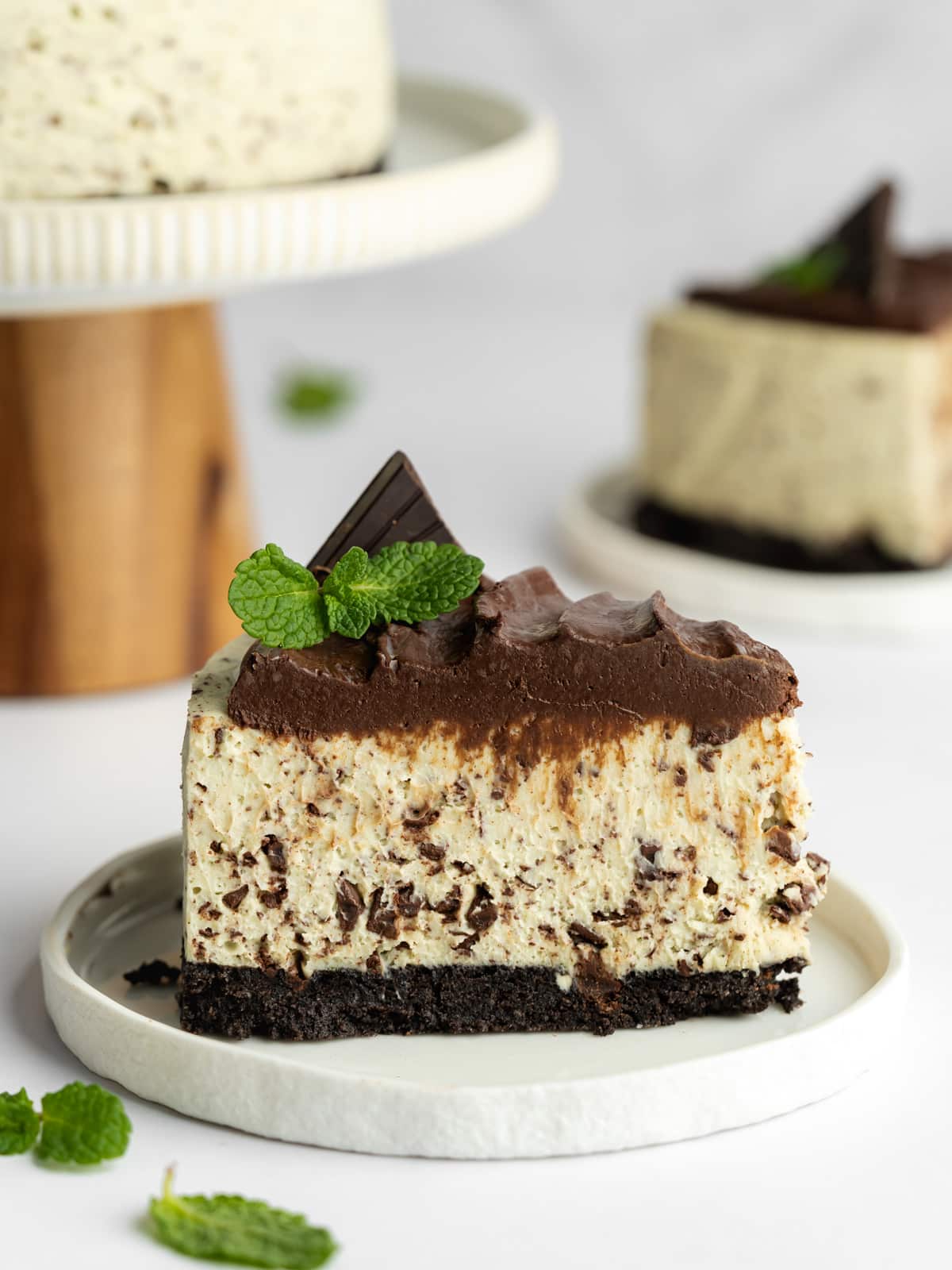 a slice of mint chocolate cheesecake with mint leaves and a piece of chocolate on top of a white plate.