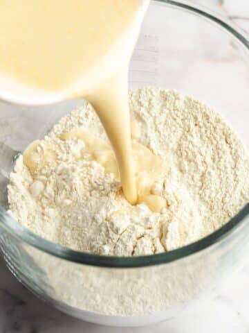 pouring wet ingredients into dry ingredients i a glass stand mixer bowl.