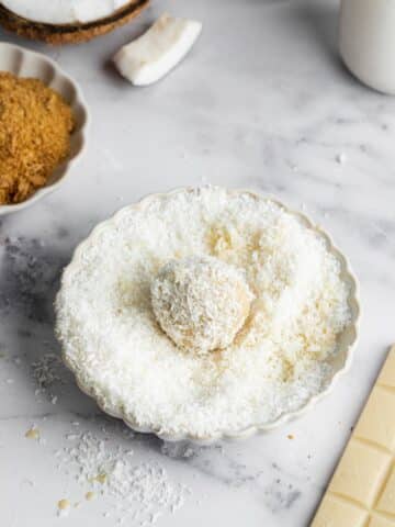 coconut truffle dipped in white chocolate being rolled in shredded coconut.