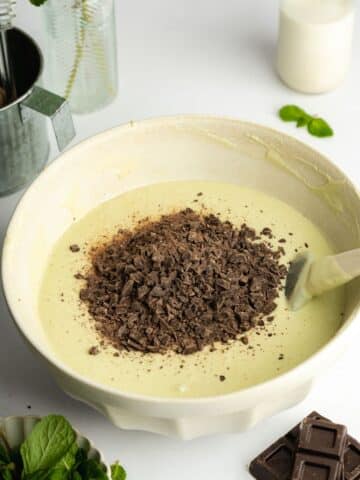 a large ceramic bowl with mint cheesecake filling and chocolate chips being folded in.