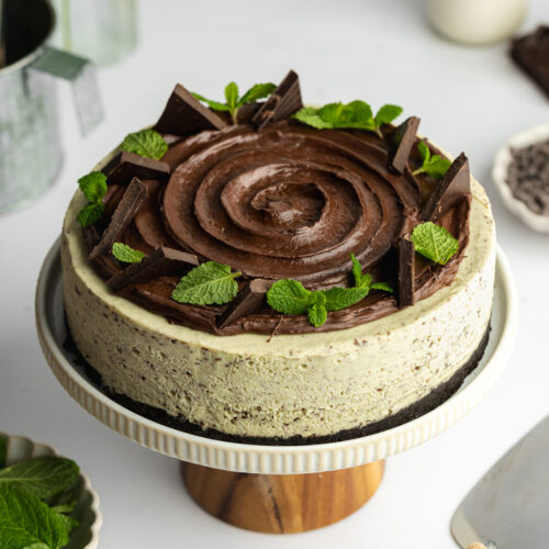 mint cheesecake with ganache topping and fresh mint leaves on a wooden cake stand.