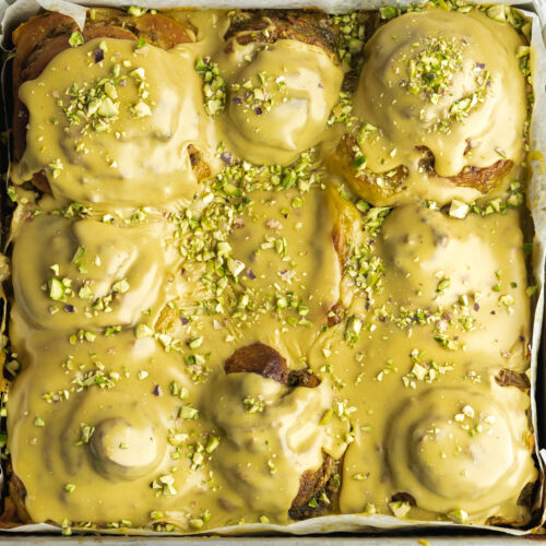 a square pan filled with pistachio cinnamon rolls covered in pistachio icing.