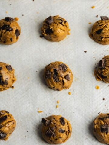 cookie dough balls on a baking sheet with extra chocolate chunks studded on top of them before baking.