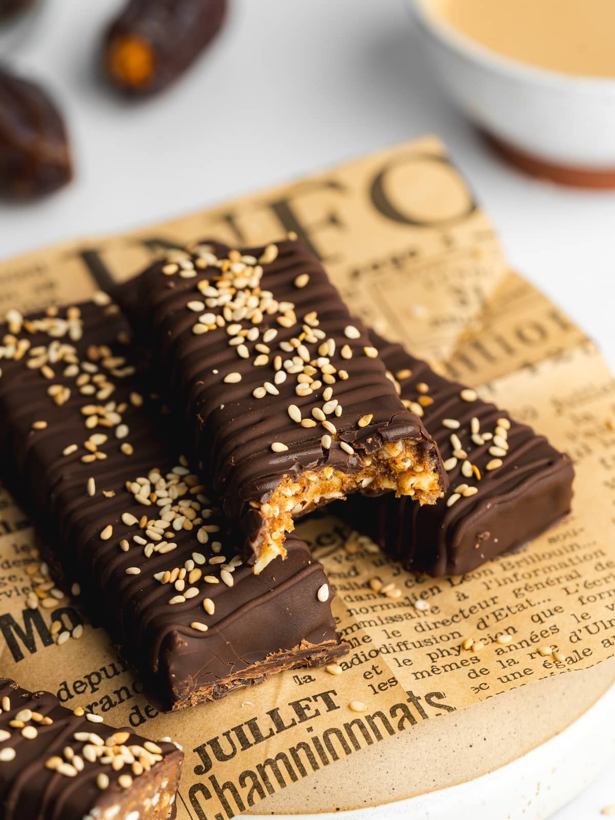three chocolate coated date bars and the top one has a bite taken from it showing the chewy texture inside.