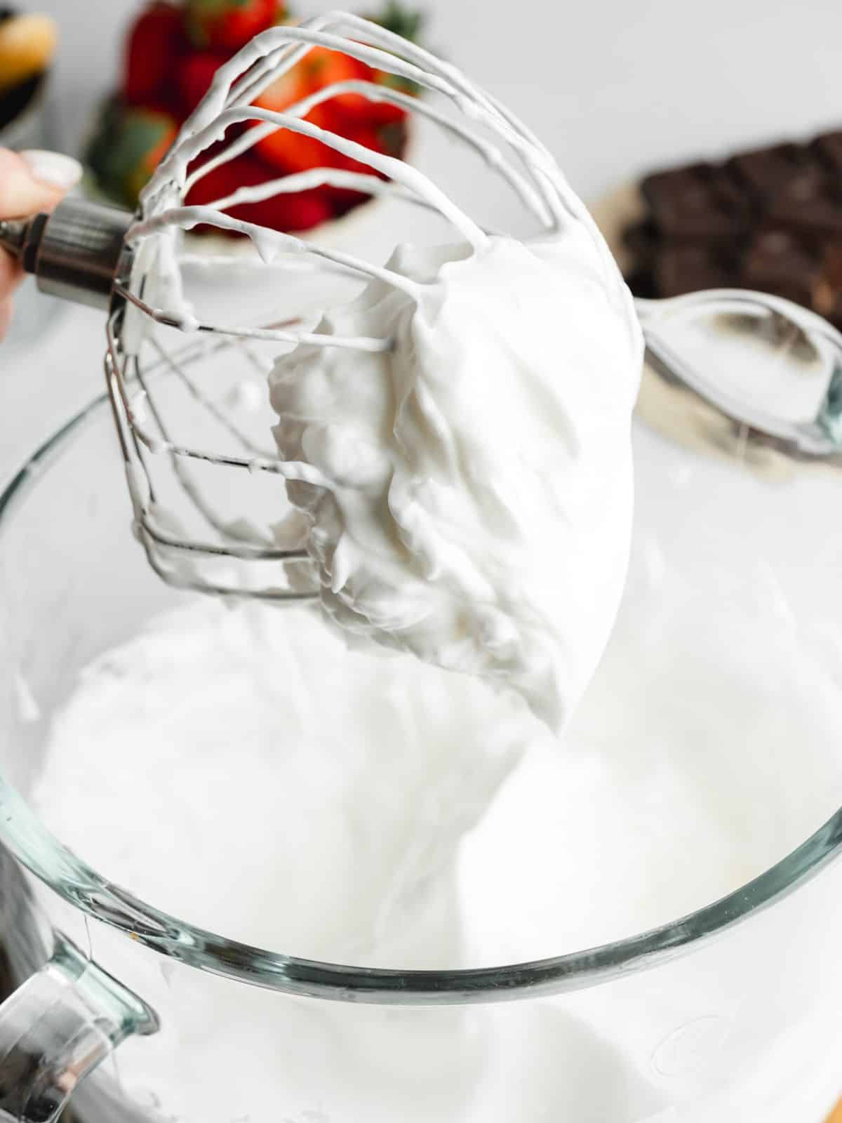 a whisk holding up whipped aquafaba that's been whisked to stiff peaks.