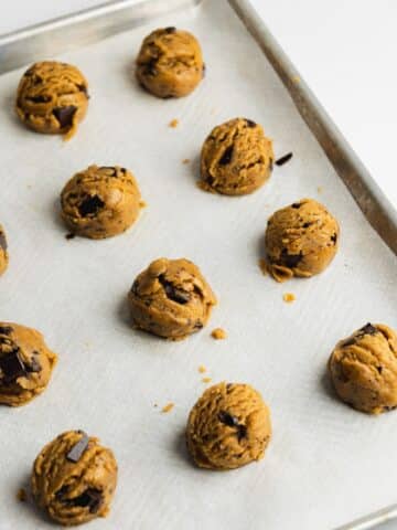 olive oil chocolate chip cookie dough scooped on a lined baking sheet.
