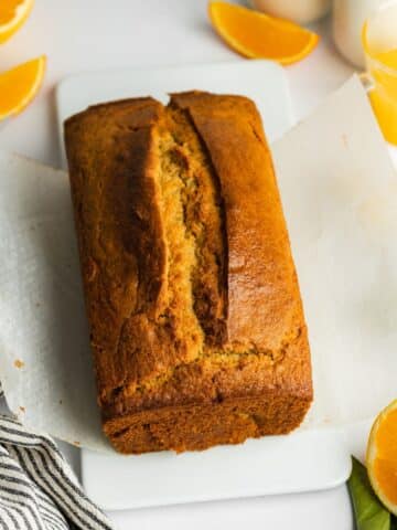 orange loaf cake cooling on a sheet of parchment paper.