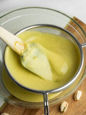 pistachio custard being passed through a fine mesh sieve to remove lumps and a vanilla pod.