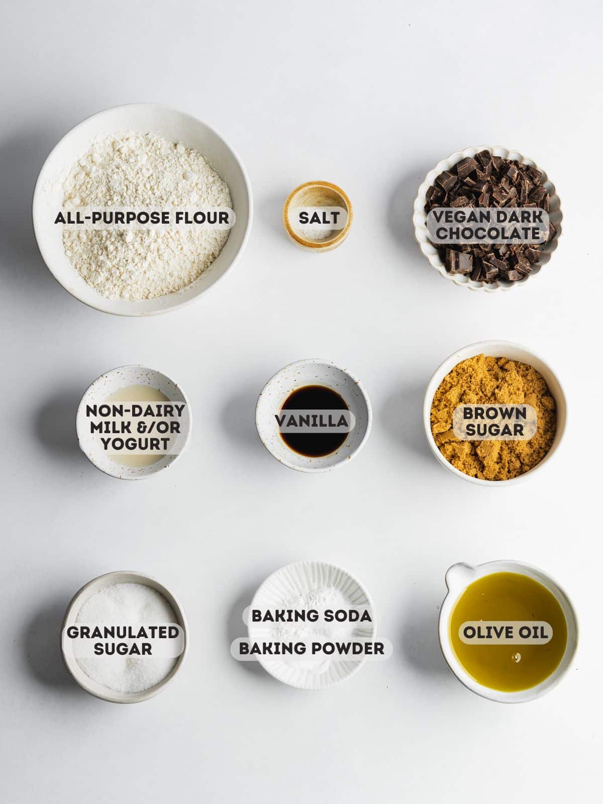 ingredients for chocolate olive oil cookies measured in bowls on a white surface.
