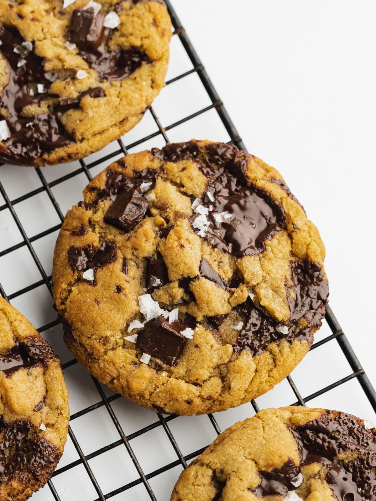freshly baked olive oil chocolate chip cookies on a black cooling rack.