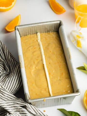 a loaf pan filled with orange cake batter and a thin strip of vegan butter down the center.