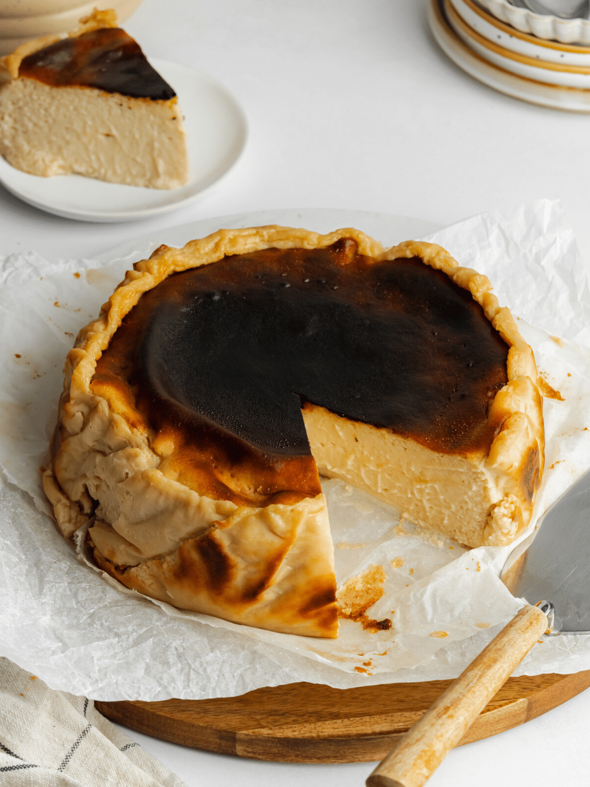 a basque cheesecake on a wooden serving board with a slice cut from it.