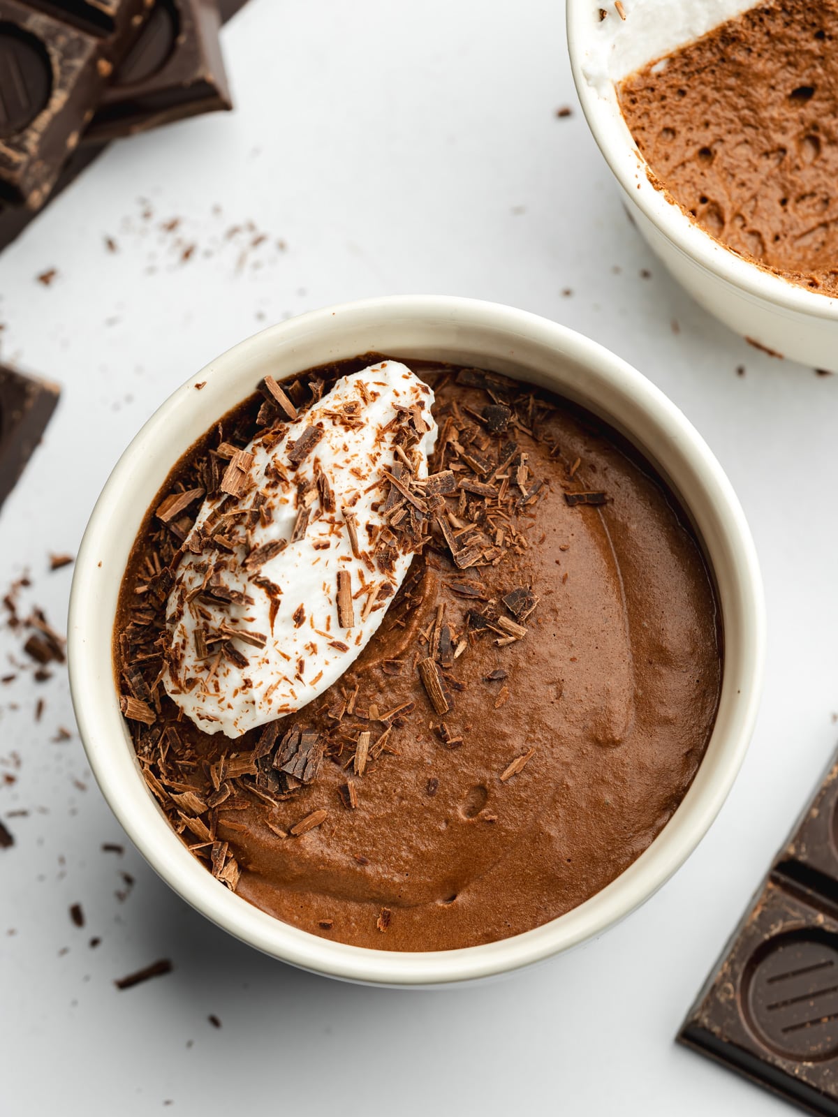 a pot of chocolate mousse served with a quenelle of dairy-free cream and dark chocolate shavings.