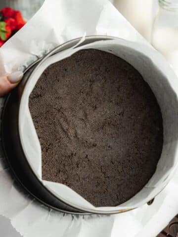 oreo cookie crust pressed into a lined cake pan.