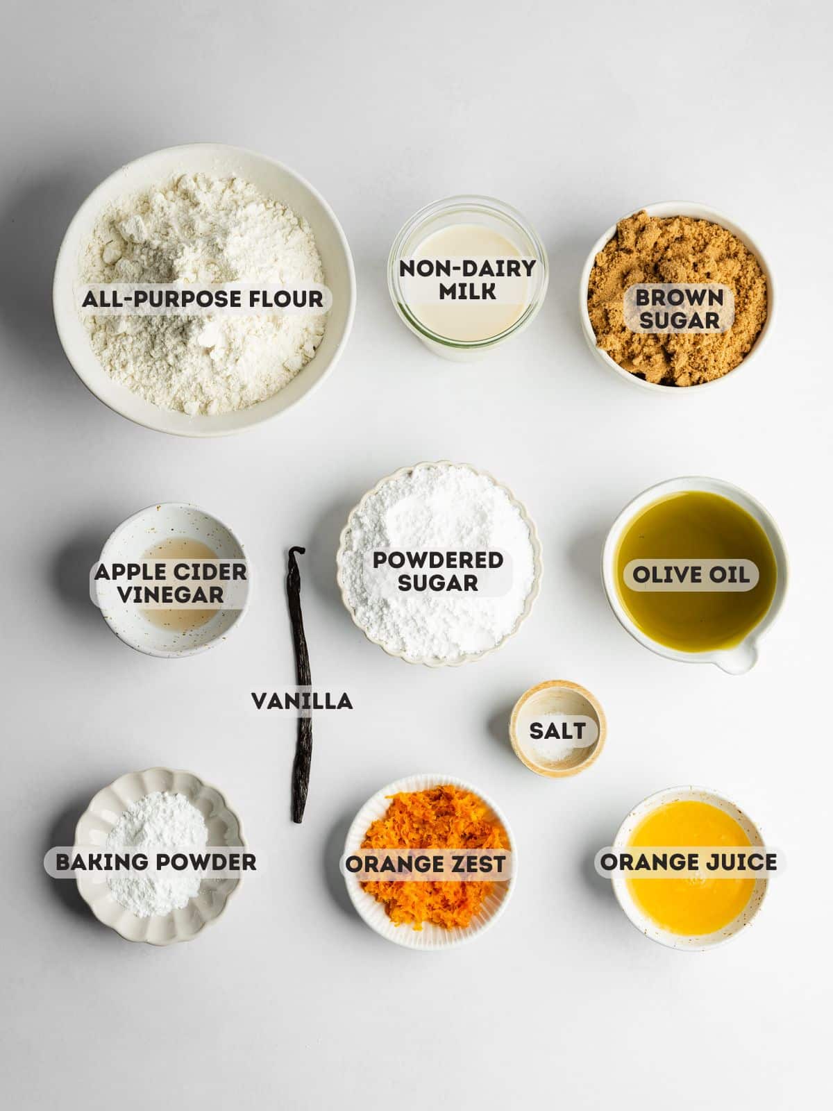 ingredients to make vegan orange loaf cake measured out in bowls on a white sruface.