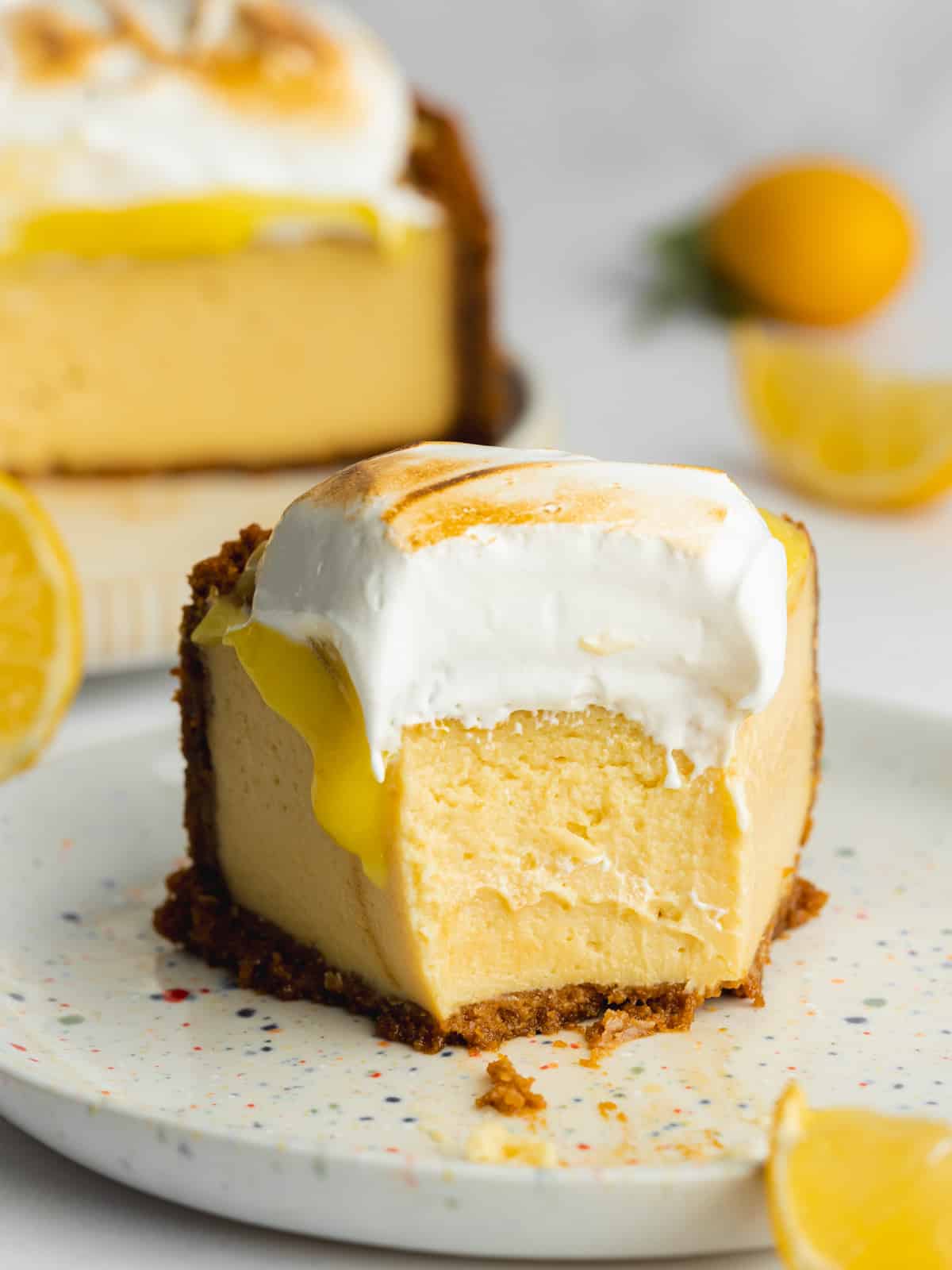 a slice of lemon meringue cheesecake on a plate with a biteful taken from it showing the creamy interior.