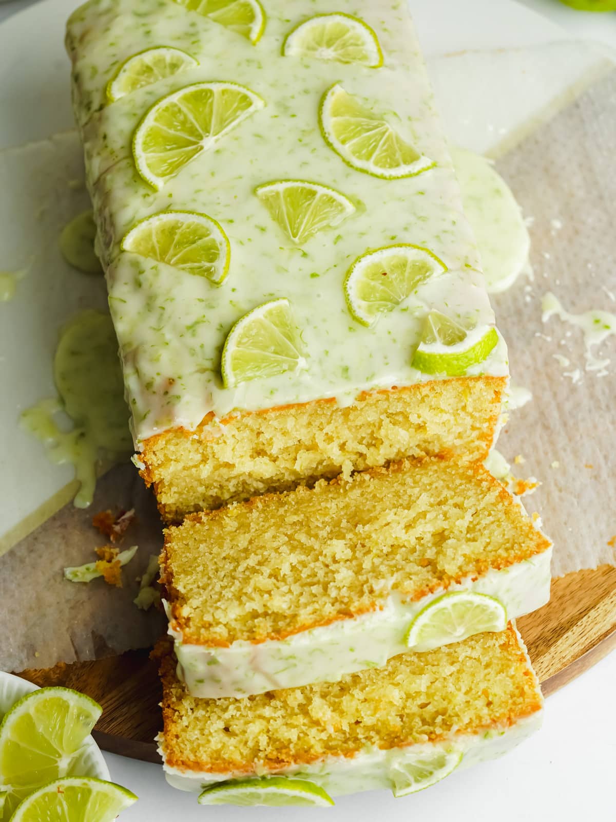 a lime cake on a wooden board with 2 slices and lime glaze on top.