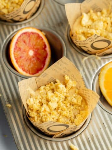 orange muffins with crumb topping in a muffin pan before bakinghg.