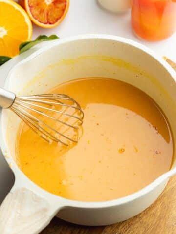 orange curd wet ingredients in a saucepan with a whisk.