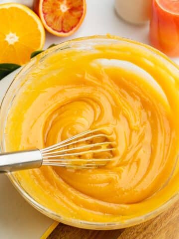 a large bowl with orange curd being whisked showing the thick consistency.