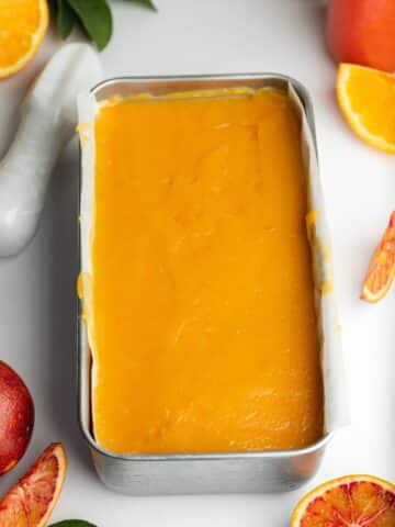 a loaf pan filled with orange cheesecake and topped with orange curd.