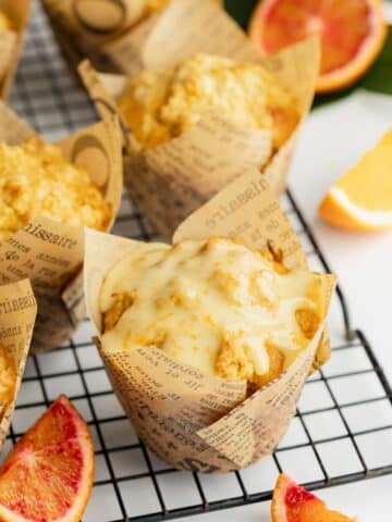 orange muffins with fresh orange sugar glaze in brown paper tulip liners on a wire rack.