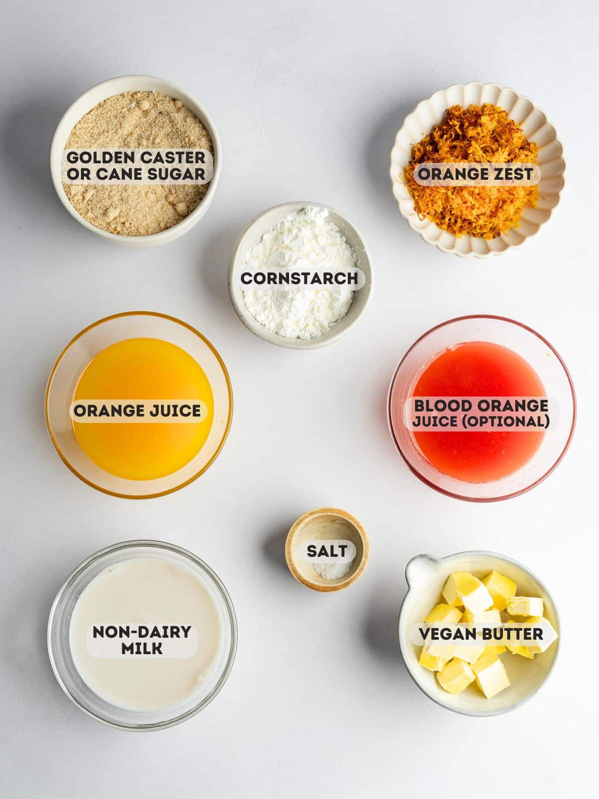 ingredients for homemade orange curd measured out in bowls on a gray surface.