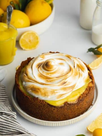 lemon curd cheesecake topped with toasted meringue with fresh lemons in the background.