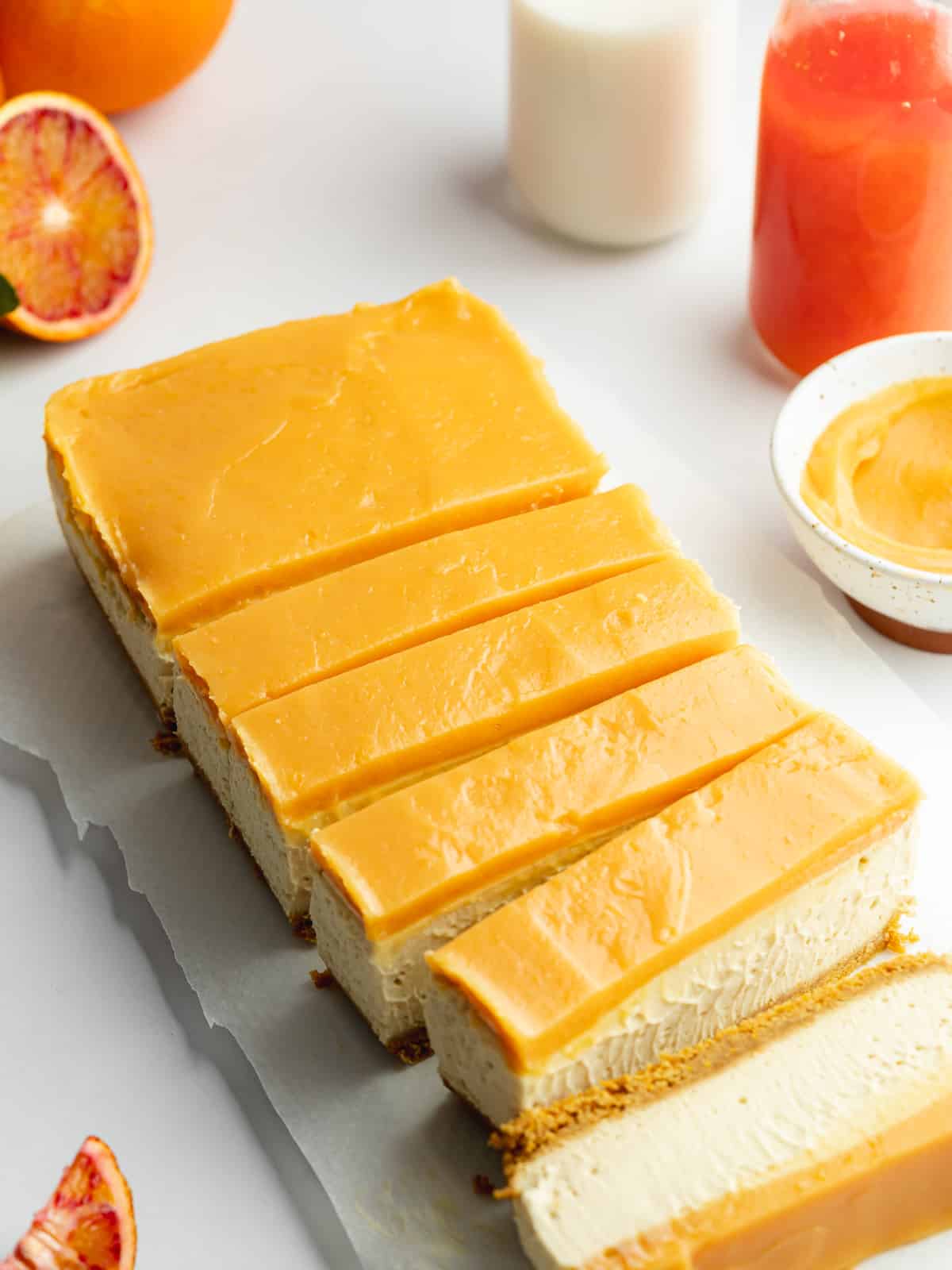 orange curd cheesecake bars sliced on a long white plate with fresh oranges scattered around.