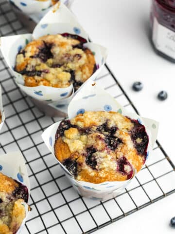 blueberry muffins with crumb topping in blueberry tulip liners on a wire rack.